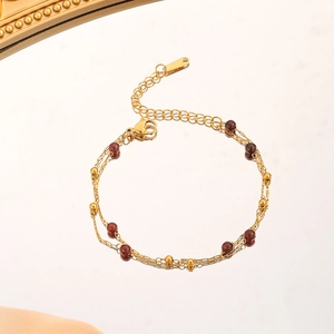 Détail de bracelet multicouche en chaîne dorée avec perles de grenat et fermoir mousqueton