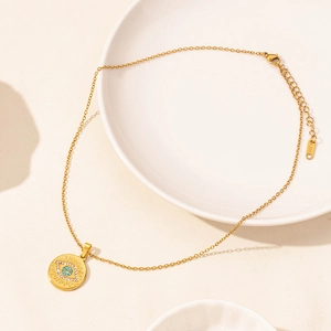 Golden stainless steel evil eye pendant necklace on a clean minimalist ceramic tray