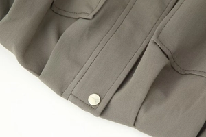 Close-up of taupe jacket fabric featuring fine stitching and a silver metal button