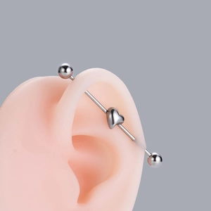 Close-up of stainless steel heart industrial barbell piercing on silicone ear model