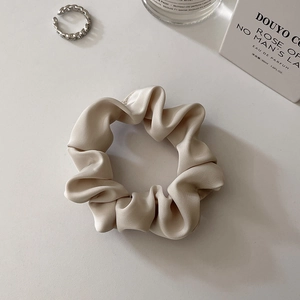 Detail of silk satin scrunchie and silver chain engraved ring on a minimalist background