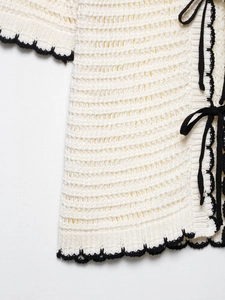 Close-up of white crochet knit top with black contrast scalloped edges and tie closure