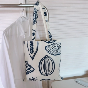 Gros plan d'un sac cabas en toile blanche avec imprimés végétaux bleus sur un cintre