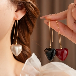 Detail of vintage heart-shaped drop earrings in beige, black, and deep red finishes