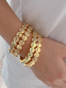 Detail of stacked gold charm bracelets with colorful crystal eyes and smiley face patterns
