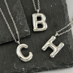 Macro shot of silver bubble letter B C H pendants on stainless steel necklaces