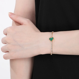 Detail of a gold bracelet with a green heart pendant and sparkling zircon stones