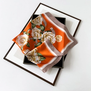 Detailed view of satin floral scarf with orange flower print on a wooden tray