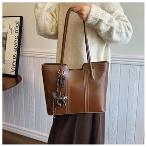 Close-up of brown leather tote bag with white contrast stitching and cat charm detail