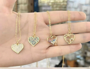 Dettaglio di quattro ciondoli a cuore in oro 14k con zirconi colorati tenuti in mano