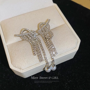 Macro detail of silver tassel earrings with zircon knots and pearls in a beige jewelry box