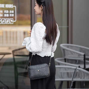 Detail view of a black quilted crossbody bag featuring V-pattern stitching and gold hardware