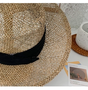 Detail shot of the woven seagrass texture and black ribbon on a summer beach sun hat