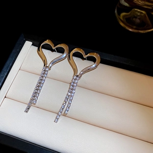Detailed close-up of golden heart earrings with sparkling rhinestone tassels on beige box