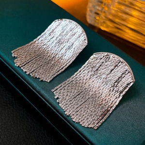 Silver metallic fringe tassel earrings with semi-circular polished accents on leather texture