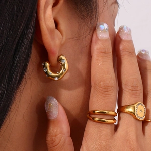 Detail showing gold C-shaped hoop earrings and elegant rings set with shiny crystals