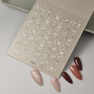 Close-up of 5D embossed nail stickers with white floral patterns and silver accents