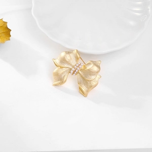 Elegant golden bow brooch with silk texture and vertical pearl inlay on white tray