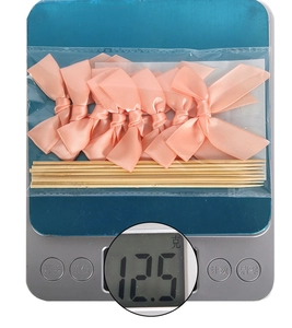 Close-up of pink ribbon bow cake toppers in a bag weighing 12.5g on a digital scale