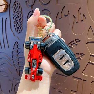 Miniature red formula car keychain with golden metal ring and textured wood background