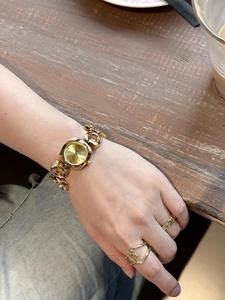 Golden hollow chain watch on wrist with round Hera dial and lifestyle coffee background