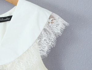 Macro view of white V-neck dress featuring delicate eyelash lace trim and branding label