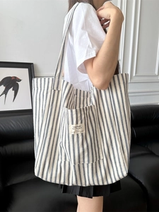 Large striped canvas tote bag shown on model with shoulder strap and outer pocket