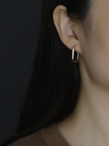 Macro shot of minimalist silver rectangular geometric hoop earring worn on model earlobe