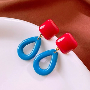 Detail of vintage square red and teardrop blue earrings on a white ceramic plate