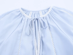 Detailed neckline of light blue blouse featuring lace panels and drawstring ties