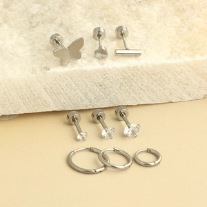Set of 9 silver stainless steel earrings featuring studs and hoops on a white stone base