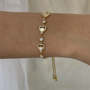 Detail of adjustable 18K gold heart bracelet with shell inlay and zircon accents
