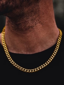 Close-up of a golden Cuban link necklace worn by a model with a dark focused background