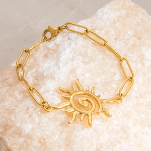 Detailed view of a gold sun pendant bracelet on a textured rock for a trendy aesthetic