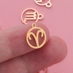 Golden Aries constellation pendant in stainless steel held on a fingertip for size view