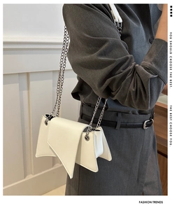 Detail of white asymmetric triangular flap bag with silver chain strap and accordion sides