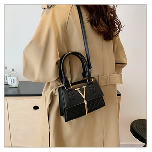 Detail of black leather handbag featuring metal V-buckle and elegant tassel charm