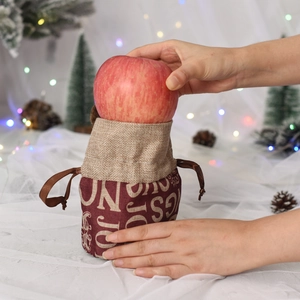Person holding a burgundy drawstring Christmas gift bag for apples with warm holiday lights