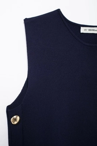 Detail view of dark blue knit vest neckline and side gold button feature