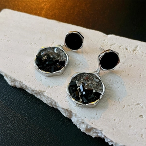 Détails de boucles d'oreilles géométriques sombres avec cristaux sur support pierre