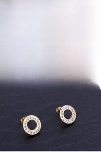 Macro shot of gold circular earrings with white pavé crystals on a black texture