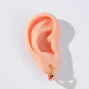 Close-up of gold stainless steel hoop earring with pink evil eye charm on model ear