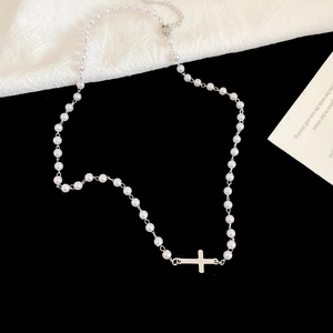 Close-up of pearl necklace featuring a polished silver cross pendant on black background