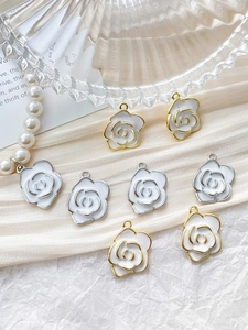 Detailed view of 14k gold-plated camellia flower pendants with white enamel on fabric