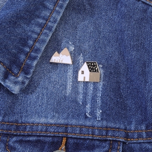 Close-up of enamel house and snow mountain brooches pinned on denim jacket lapel