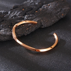 Close-up of rose gold twisted geometric open bangle on a textured black charcoal base