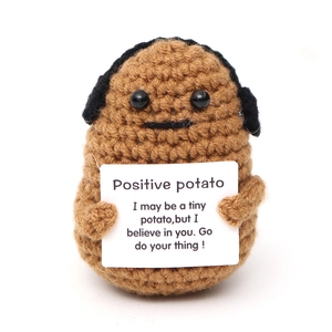 Detail of handmade crochet potato doll holding a positive message card on white backdrop