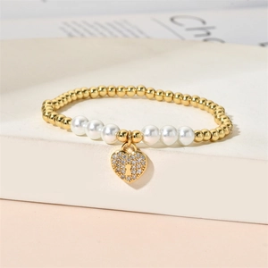 Macro view of gold beaded bracelet with white pearls and a crystal heart padlock charm