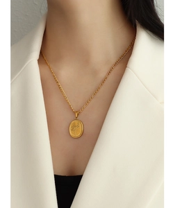 Détail du pendentif ovale doré avec gravure de rose sur une chaîne Figaro classique