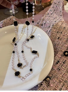 Close-up of layered necklace with white pearls and black stones on tweed fabric